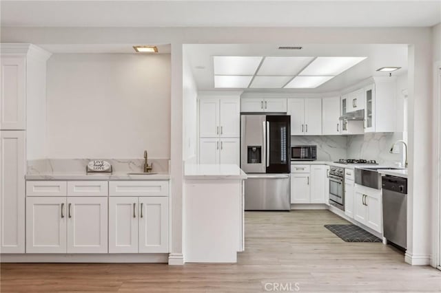 kitchen featuring stainless steel appliances, under cabinet range hood, a sink, and white cabinetry