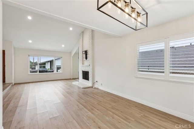 unfurnished living room featuring baseboards, lofted ceiling, a brick fireplace, and light wood-type flooring