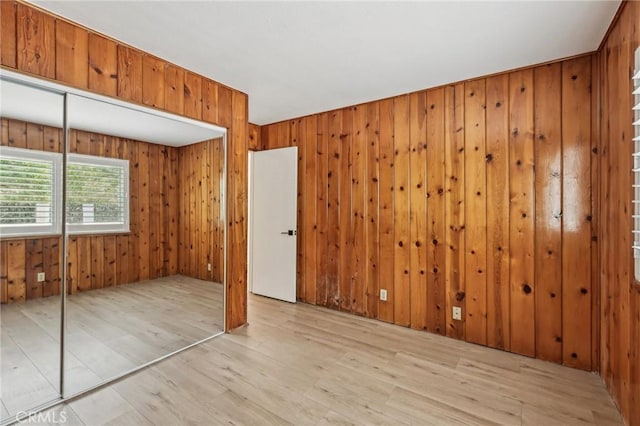 unfurnished bedroom with wooden walls, a closet, and light wood finished floors