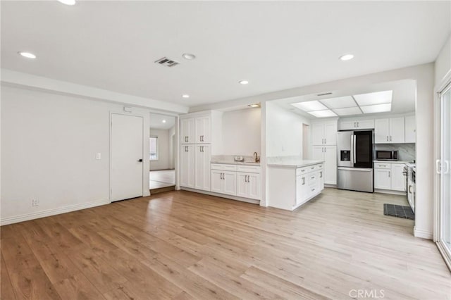 kitchen featuring light wood-style flooring, light countertops, white cabinetry, and appliances with stainless steel finishes