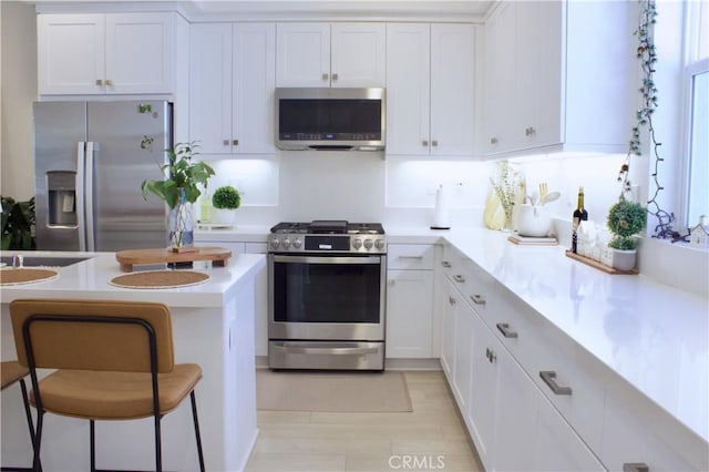kitchen featuring white cabinets, stainless steel appliances, light countertops, and a kitchen bar
