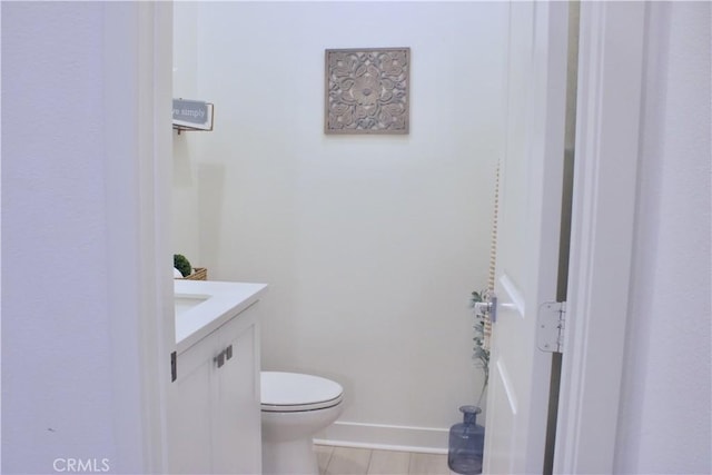 half bath featuring baseboards, vanity, tile patterned flooring, and toilet