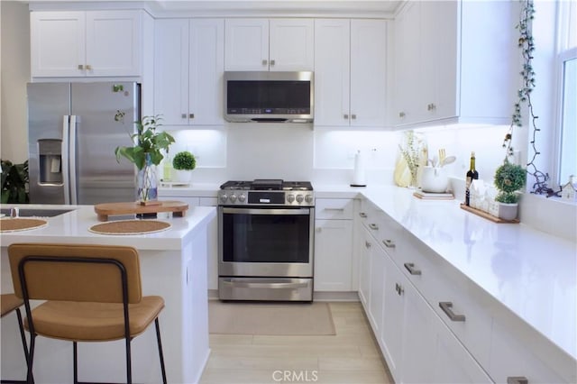kitchen featuring white cabinets, light countertops, a kitchen bar, and appliances with stainless steel finishes