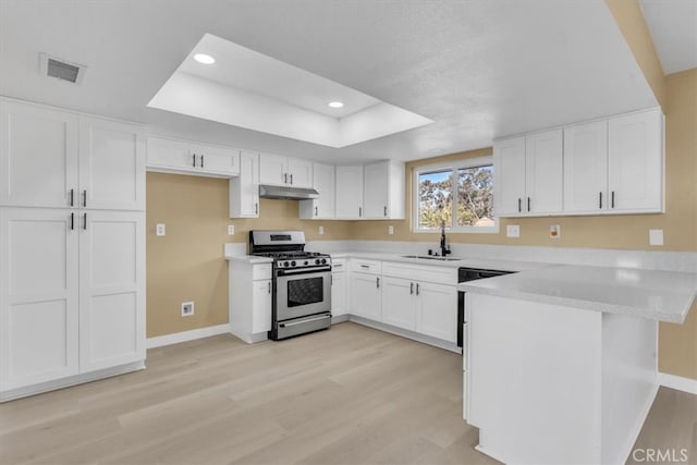 kitchen featuring under cabinet range hood, a peninsula, stainless steel range with gas stovetop, and baseboards