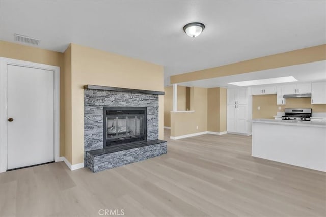 unfurnished living room with baseboards, light wood-style floors, visible vents, and a fireplace