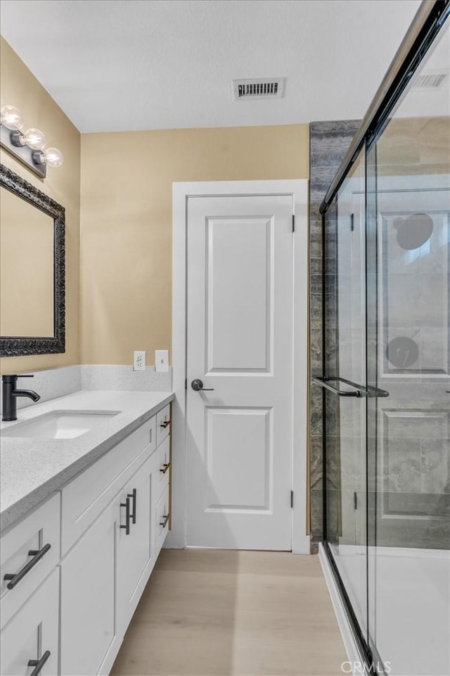 full bathroom featuring visible vents, vanity, wood finished floors, and a shower stall
