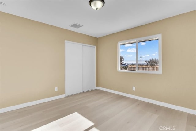 unfurnished bedroom featuring baseboards, wood finished floors, visible vents, and a closet
