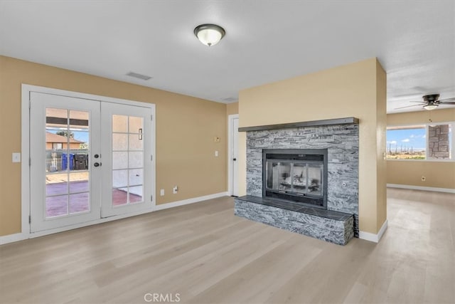 unfurnished living room with a stone fireplace, visible vents, wood finished floors, baseboards, and ceiling fan