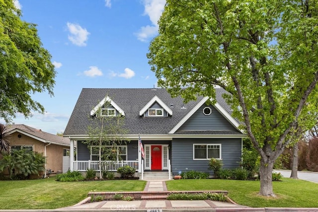 view of front facade featuring roof with shingles, covered porch, and a front yard