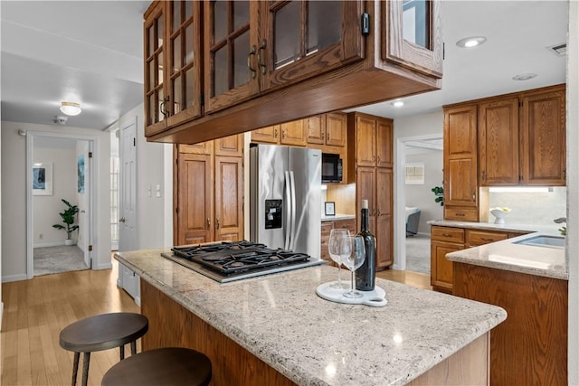 kitchen with light stone counters, a sink, light wood-type flooring, stainless steel appliances, and visible vents
