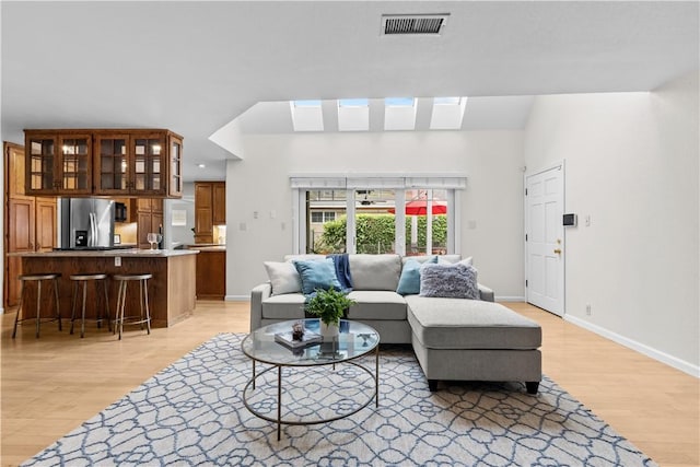living area featuring baseboards, a skylight, visible vents, and light wood-style flooring