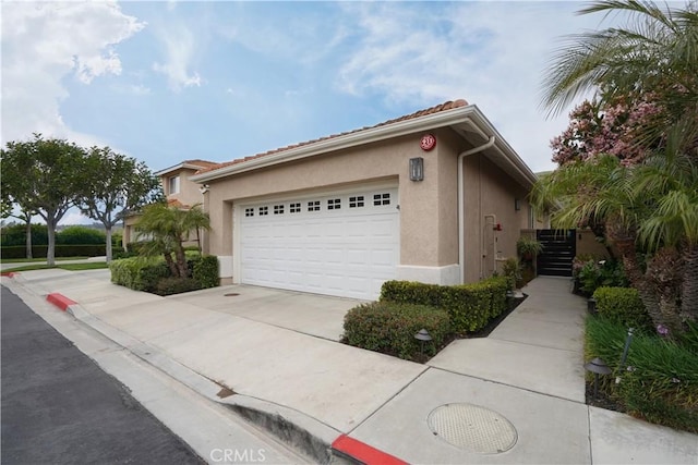 view of side of home with a garage, a tile roof, concrete driveway, and stucco siding