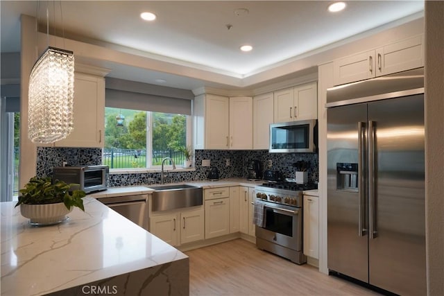 kitchen with a sink, a toaster, premium appliances, backsplash, and light stone counters