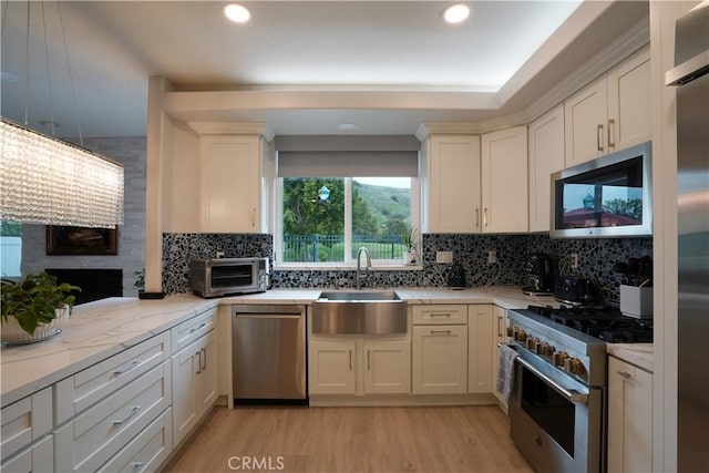 kitchen with recessed lighting, light wood finished floors, a sink, high quality appliances, and decorative backsplash