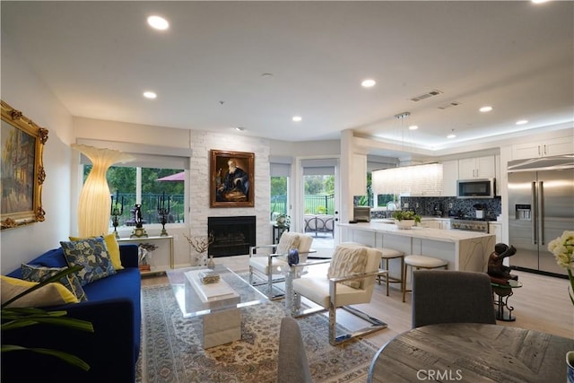 living area featuring a fireplace, a wealth of natural light, visible vents, and light wood-style flooring