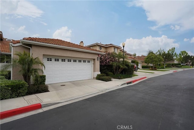 view of front of house with a tile roof, driveway, a garage, stucco siding, and a residential view