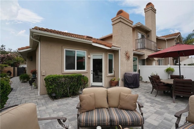 back of property with a chimney, fence, a balcony, a patio area, and an outdoor living space