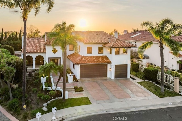 mediterranean / spanish-style house featuring an attached garage, a tiled roof, driveway, and stucco siding