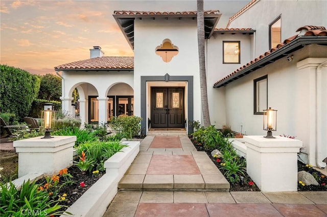 entrance to property featuring a chimney, a tile roof, and stucco siding
