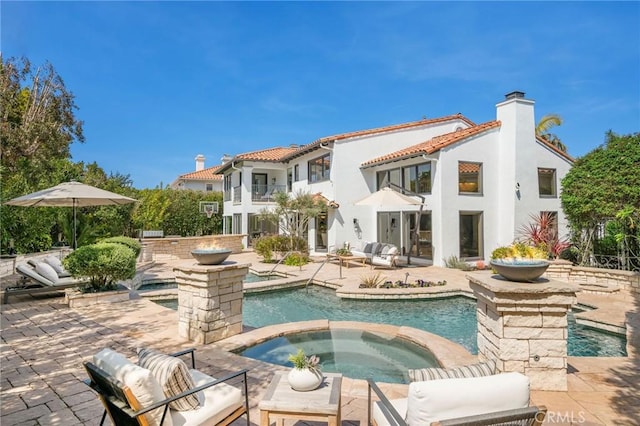 rear view of house with a tile roof, an in ground hot tub, a patio, an outdoor pool, and stucco siding