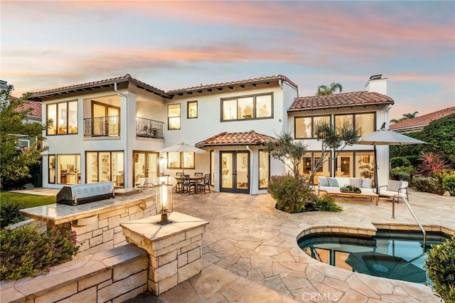 back of house at dusk featuring an outdoor kitchen, a patio area, french doors, and a balcony