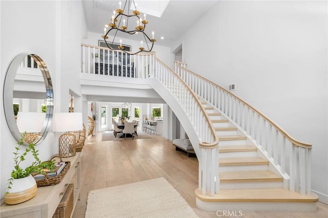 entryway featuring stairs, hardwood / wood-style floors, a high ceiling, a notable chandelier, and visible vents