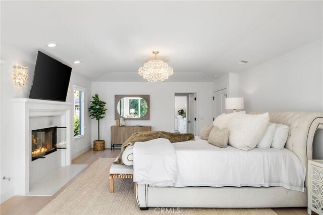 bedroom featuring radiator, a fireplace with flush hearth, wood finished floors, baseboards, and a chandelier