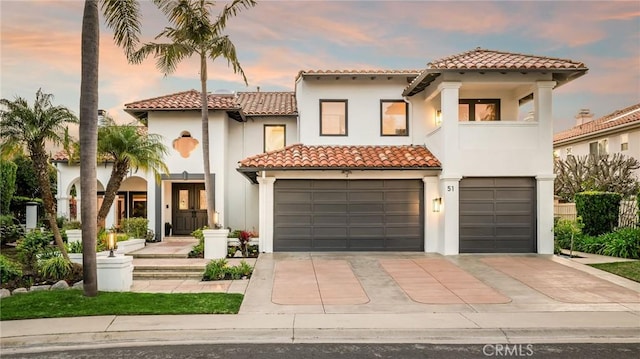 mediterranean / spanish-style house with an attached garage, a tiled roof, and stucco siding