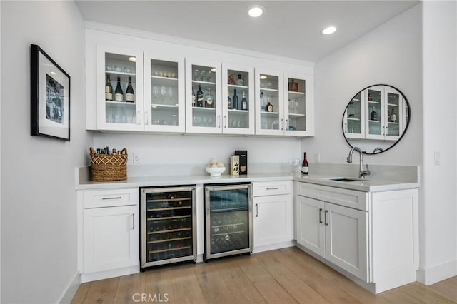 bar with a dry bar, beverage cooler, a sink, and light wood-style floors