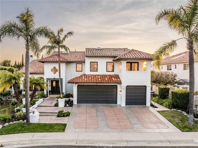 mediterranean / spanish home with a garage, driveway, a tiled roof, and stucco siding