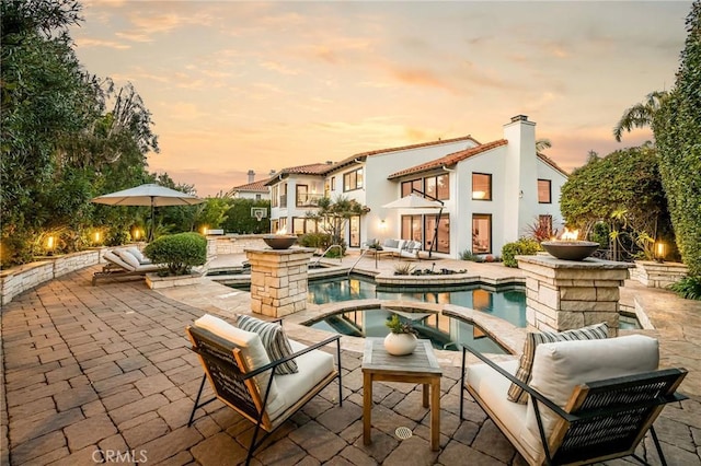 back of house at dusk with an outdoor living space, a balcony, an outdoor pool, a patio, and an in ground hot tub