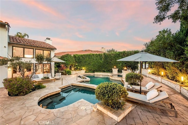 pool at dusk with a patio area, outdoor lounge area, and a pool with connected hot tub