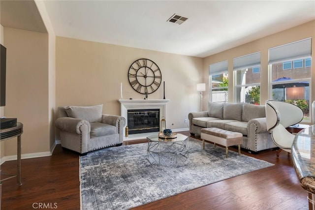 living room featuring baseboards, visible vents, a glass covered fireplace, and dark wood-type flooring