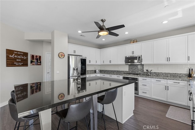 kitchen with a kitchen breakfast bar, ceiling fan, appliances with stainless steel finishes, and dark wood-type flooring