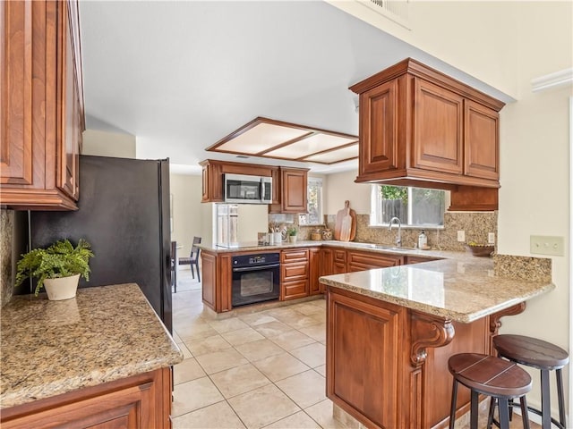 1523 E Pryor Dr, Fresno, CA 93720 - kitchen featuring a peninsula, light tile patterned flooring, decorative backsplash, brown cabinets, and black appliances