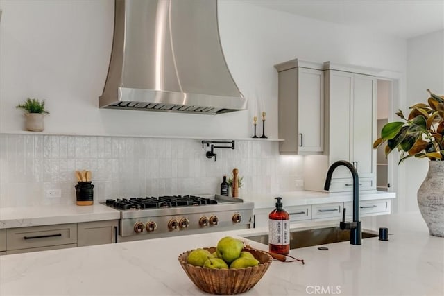 kitchen with a sink, backsplash, wall chimney range hood, and light stone countertops