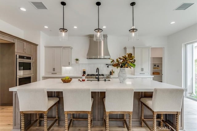 kitchen with double oven, decorative backsplash, visible vents, and wall chimney range hood