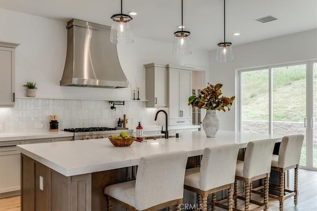 kitchen with stainless steel gas cooktop, backsplash, a sink, and wall chimney exhaust hood