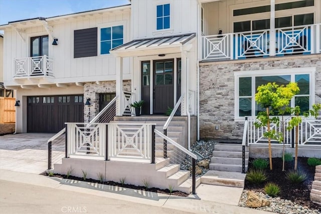view of front facade featuring an attached garage, stone siding, a balcony, covered porch, and driveway