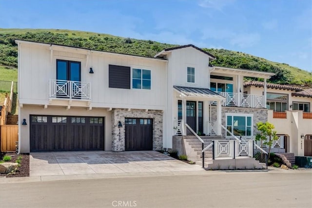 view of front of home featuring an attached garage, driveway, stone siding, and a balcony