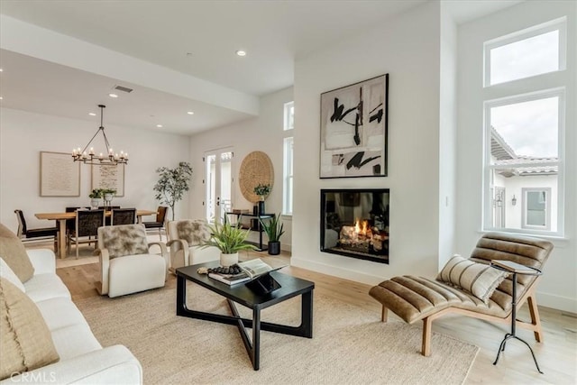 living area with a notable chandelier, a glass covered fireplace, light wood-style flooring, recessed lighting, and visible vents