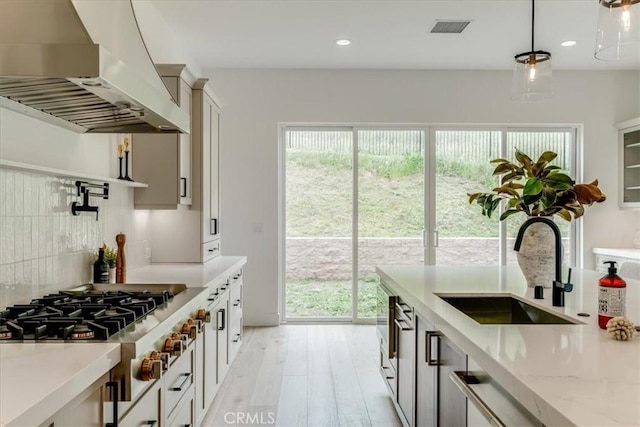 kitchen with wall chimney range hood, plenty of natural light, visible vents, stainless steel gas cooktop, and a sink