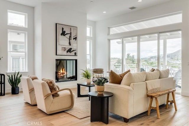 interior space with a glass covered fireplace, recessed lighting, light wood-type flooring, and visible vents