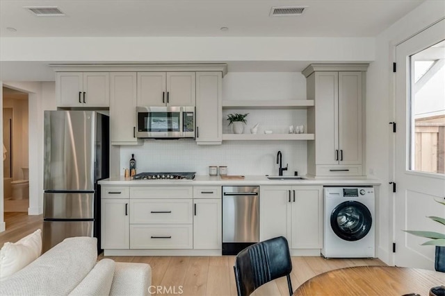 kitchen featuring visible vents, appliances with stainless steel finishes, gray cabinetry, a sink, and washer / dryer
