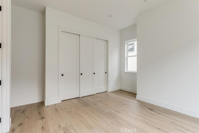 unfurnished bedroom with baseboards, a closet, and light wood finished floors
