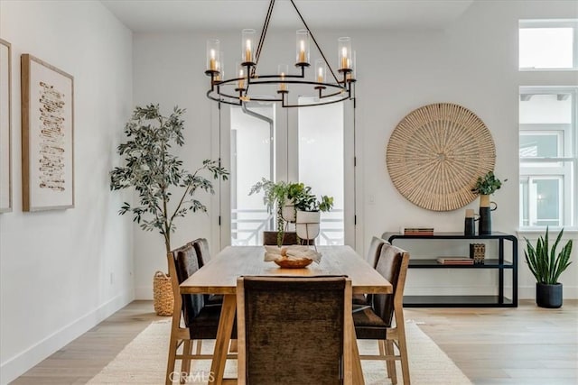 dining space with baseboards, a notable chandelier, plenty of natural light, and light wood-style floors