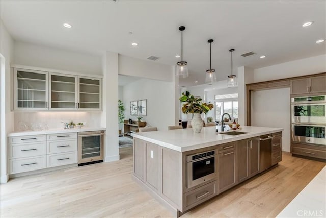 kitchen featuring light wood-style floors, a sink, beverage cooler, glass insert cabinets, and stainless steel appliances