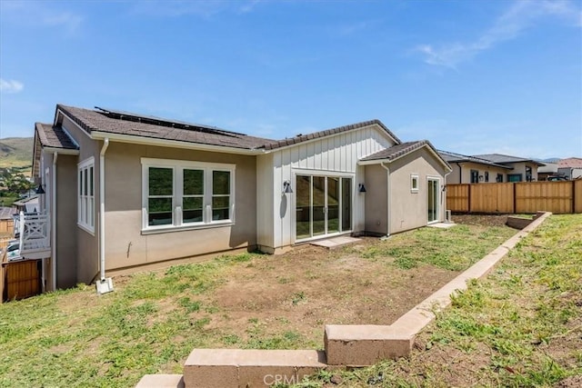 back of property with roof mounted solar panels, fence, stucco siding, and a lawn
