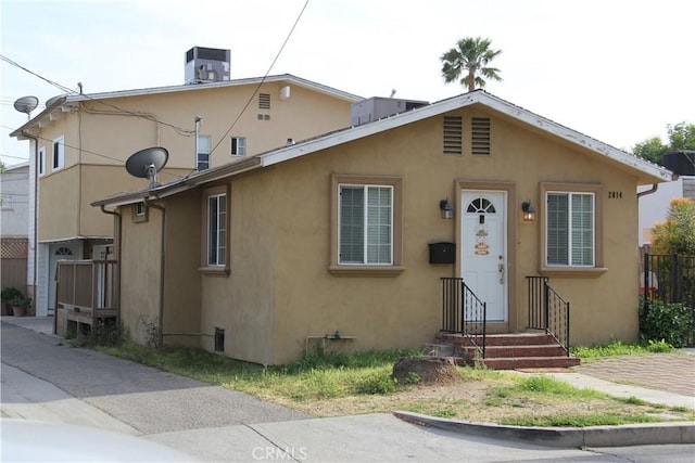 view of front of property with central air condition unit, stucco siding, and fence