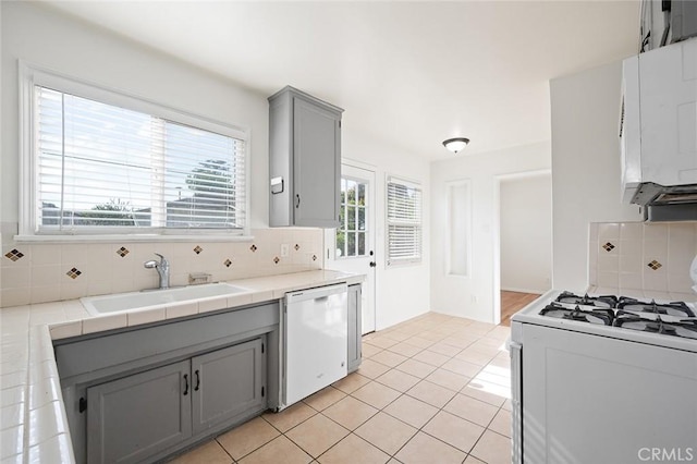 kitchen with decorative backsplash, gray cabinets, a sink, white appliances, and light tile patterned flooring